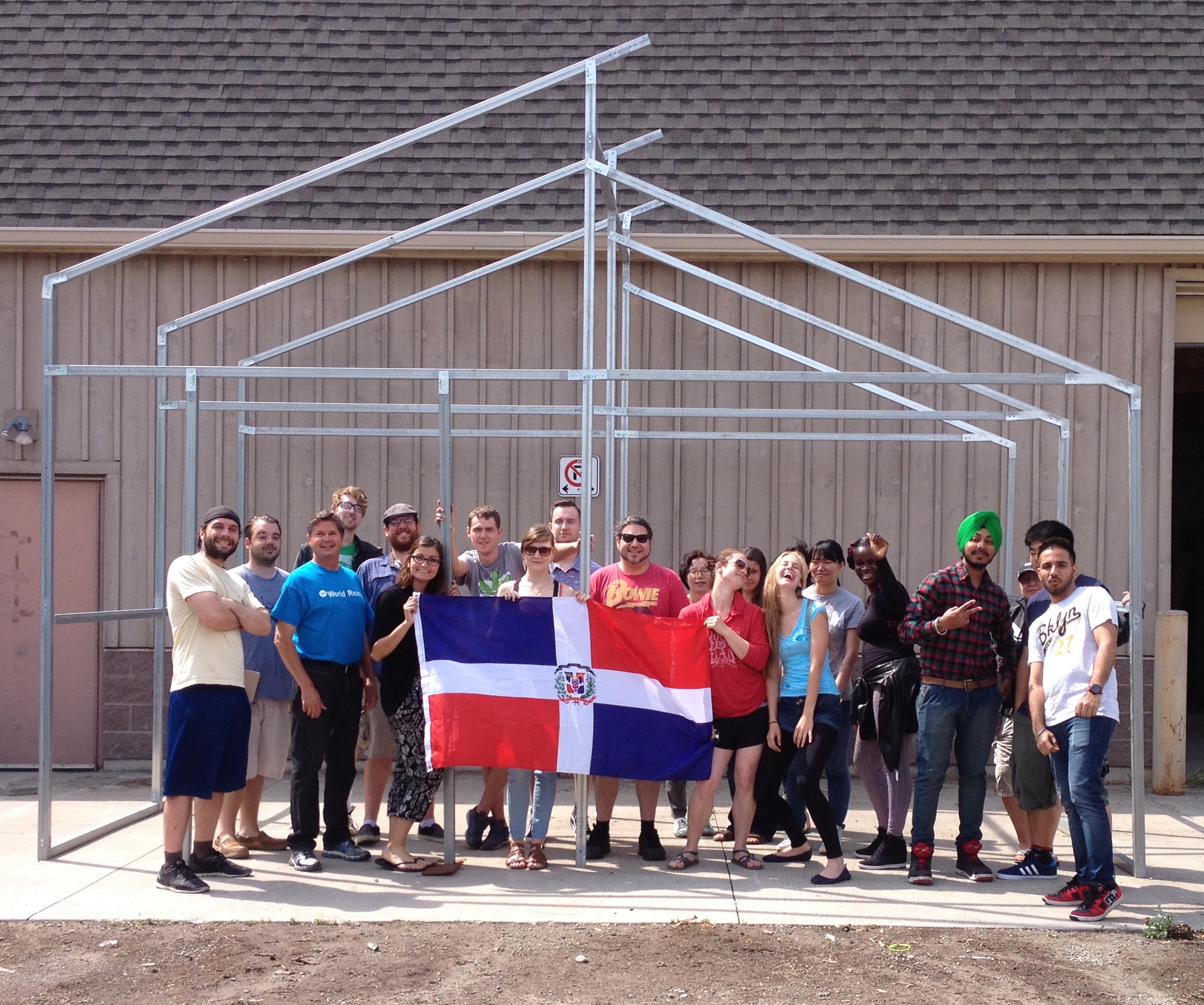 The Niagara College Horticultural Team holds up the flag of the Dominican Republic in front of a GGS Caribbean style greenhouse that is being built in Los Cacaos as part of the Be World Ready program at Niagara College